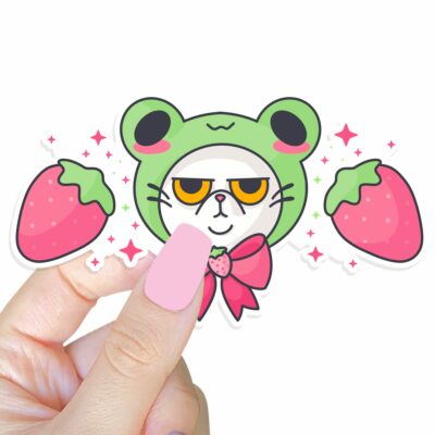 This image shows an hand-drawn adorable sticker, Grumpy Kitty with Frog Hat Sticker, which is available to purchase from HunnieByte.com