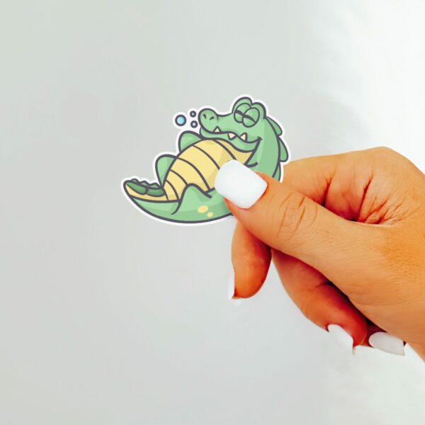 This image shows an hand-drawn adorable sticker, Lenny The Gator Sleeping Sticker, which is available to purchase from HunnieByte.com