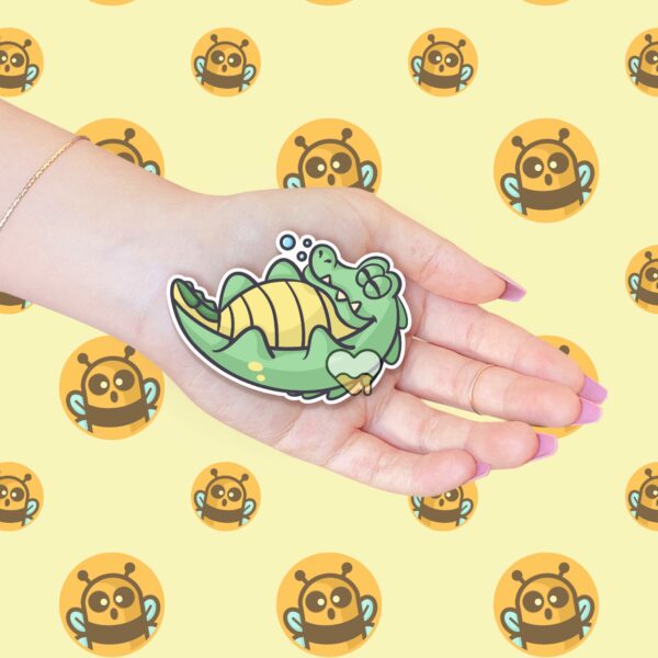 This image shows an hand-drawn adorable sticker, Lenny The Gator Sleeping Sticker, which is available to purchase from HunnieByte.com