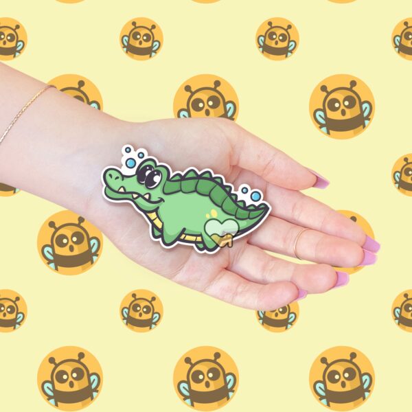 This image shows an hand-drawn adorable sticker, Lenny The Gator Swimming Sticker, which is available to purchase from HunnieByte.com