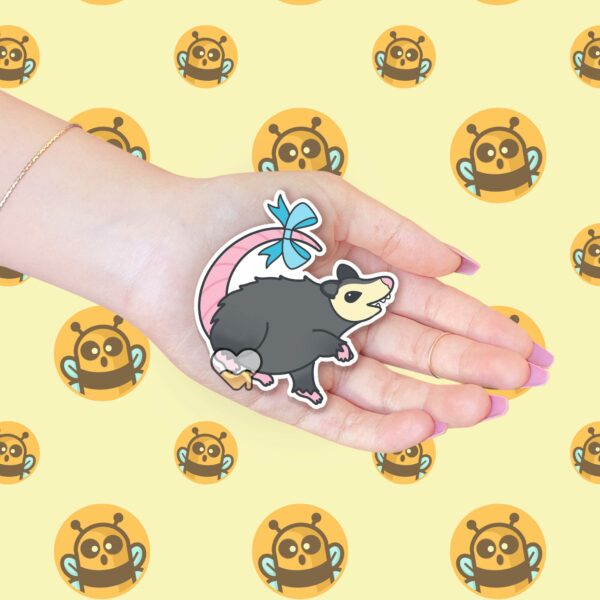 This image shows an hand-drawn adorable sticker, Possum With A Bow Sticker, which is available to purchase from HunnieByte.com